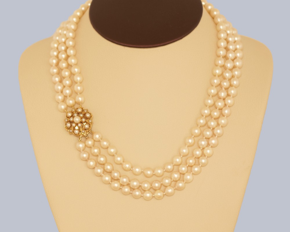 A 1960s triple strand cultured pearl necklace featuring cream-coloured pearls and a 9ct gold floral cluster clasp. View XII