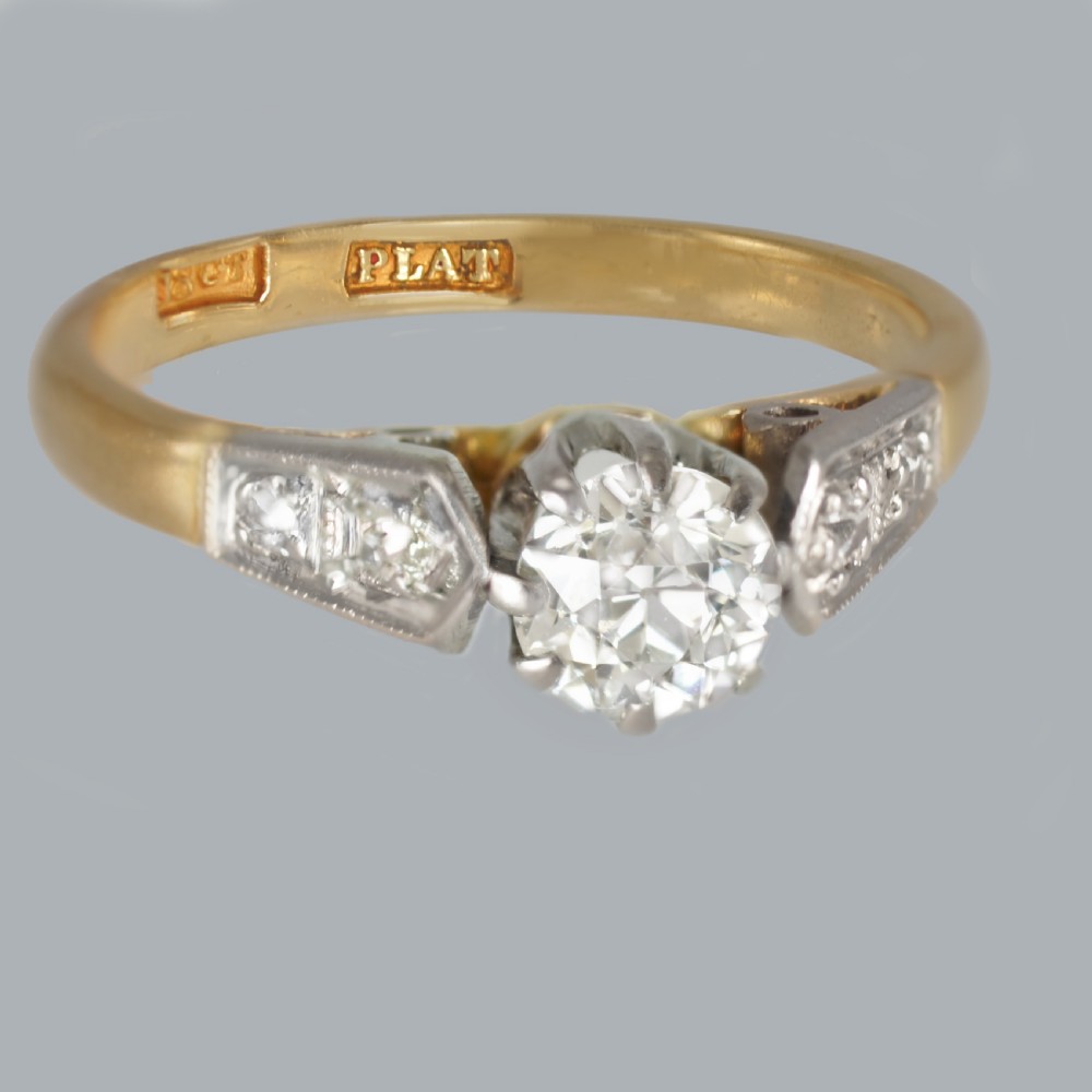 An Art Deco diamond solitaire ring featuring a round central stone set in platinum, flanked by geometric shoulders on an 18ct yellow gold band. View III