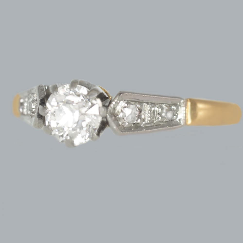 An Art Deco diamond solitaire ring featuring a round central stone set in platinum, flanked by geometric shoulders on an 18ct yellow gold band. View IV