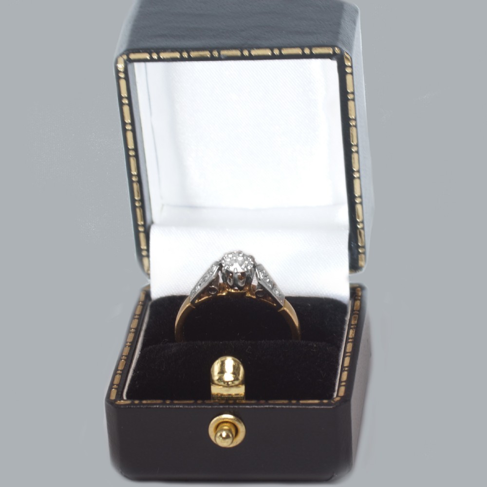 An Art Deco diamond solitaire ring featuring a round central stone set in platinum, flanked by geometric shoulders on an 18ct yellow gold band. View VII