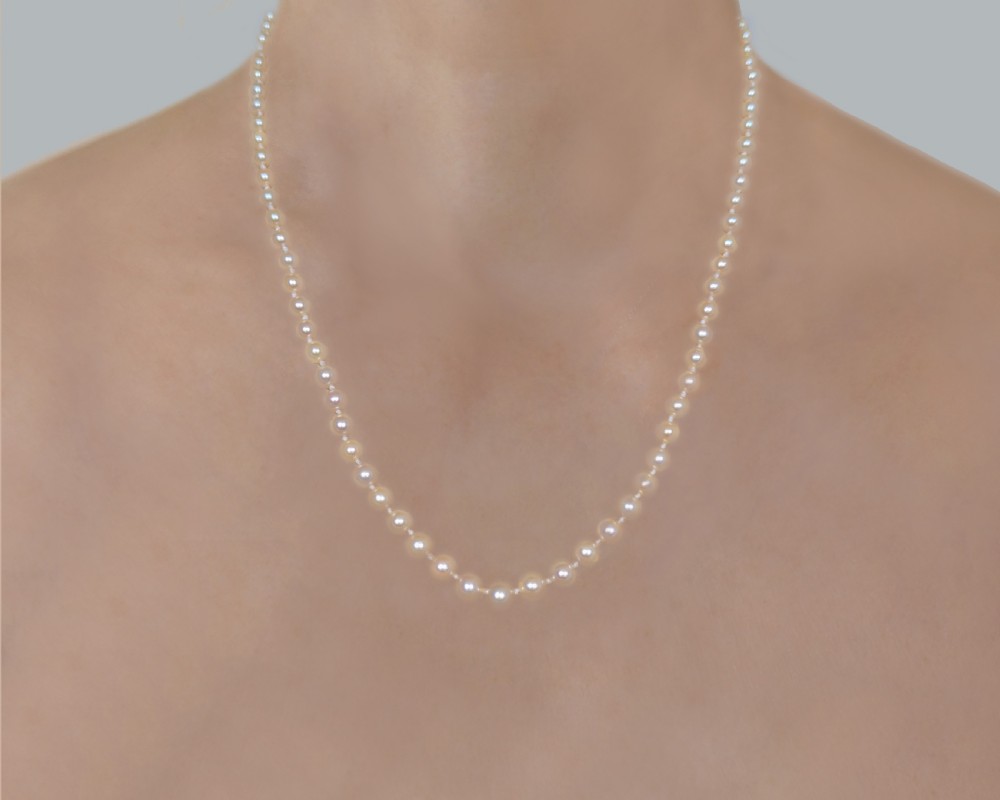 A single strand of cream pearls resting against skin, fastened around the neckline. View II