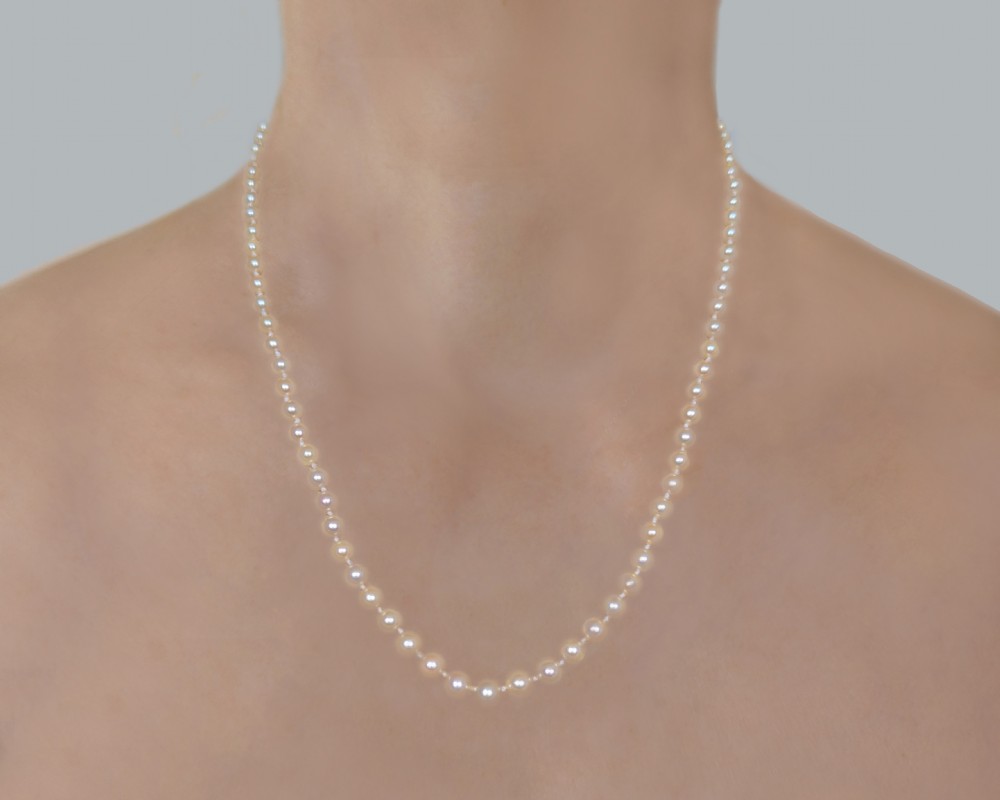 A single strand of cream pearls resting against skin, fastened around the neckline. View X