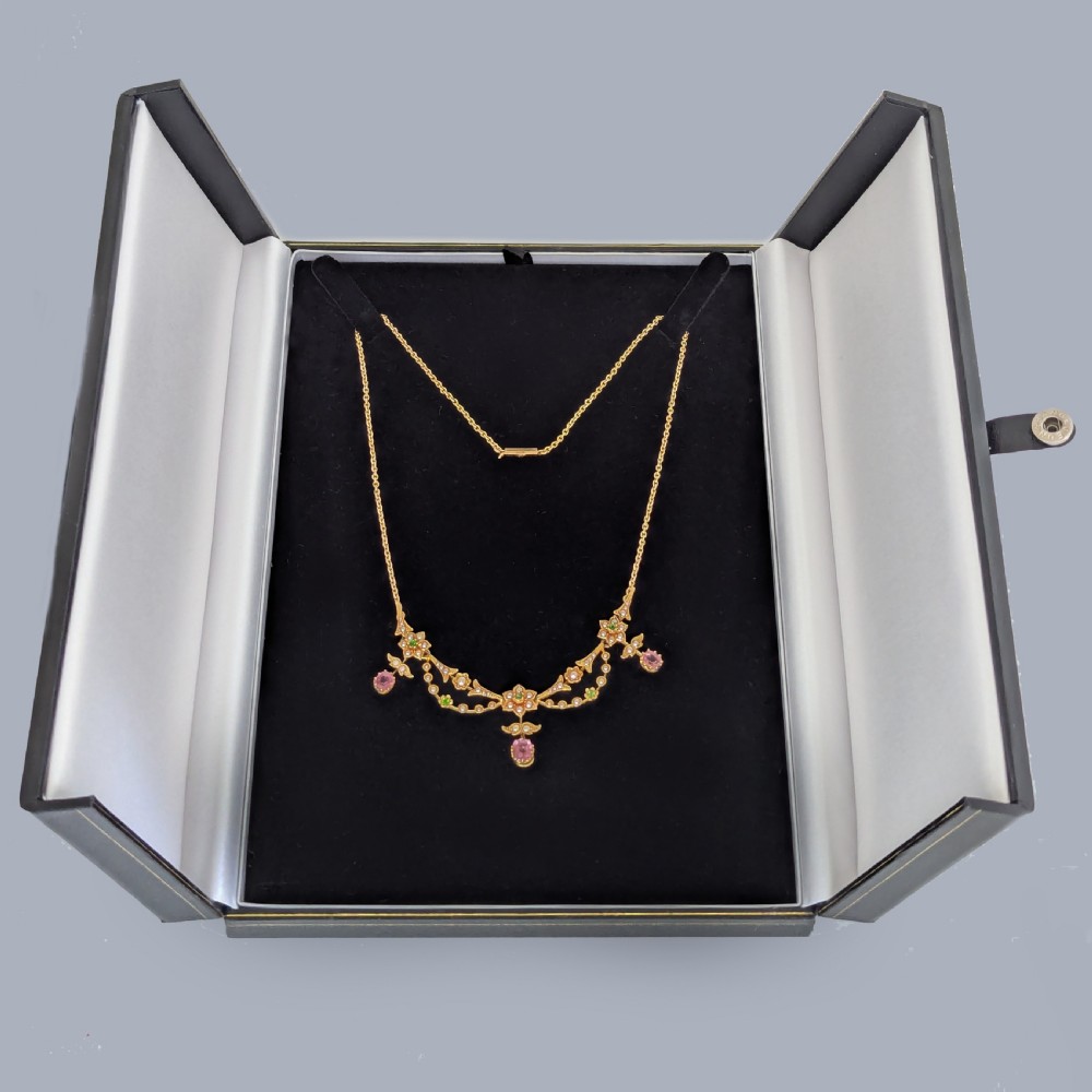An Edwardian 18ct gold festoon necklace featuring delicate seed pearl floral motifs, small green garnets, and three oval pink sapphire drops. View VII