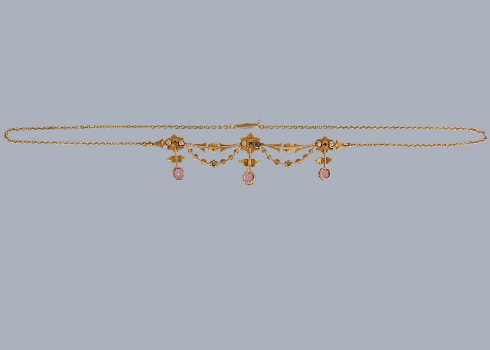 An Edwardian 18ct gold festoon necklace featuring delicate seed pearl floral motifs, small green garnets, and three oval pink sapphire drops. View IX