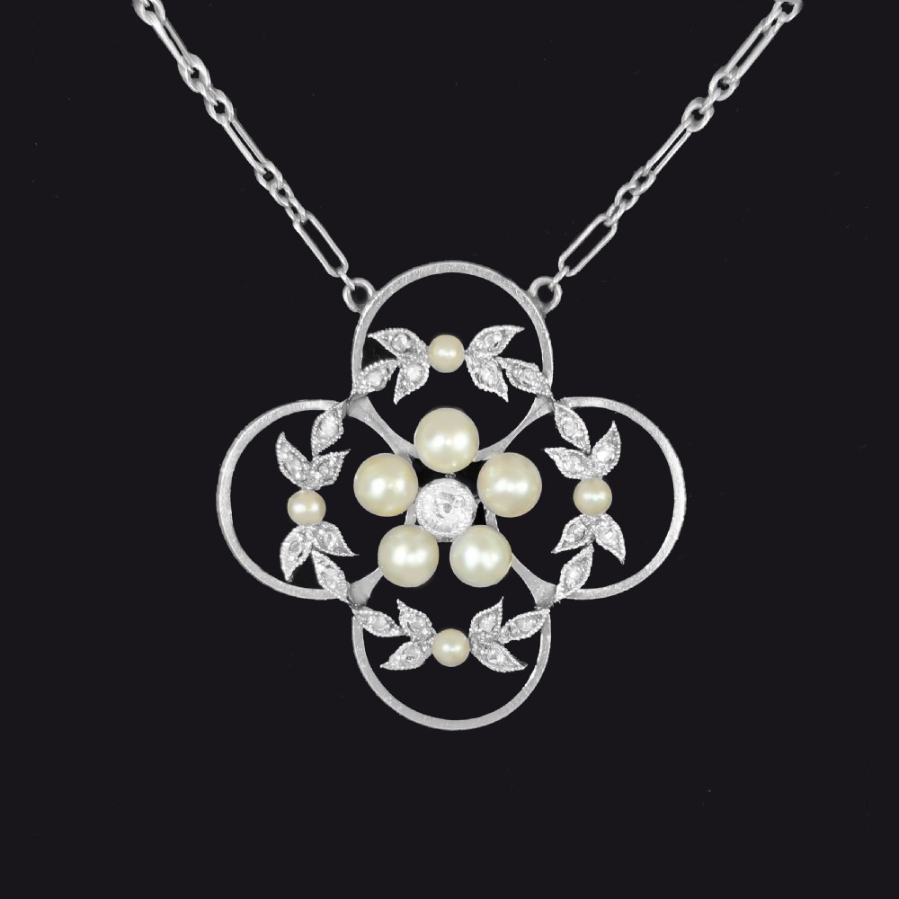 An Edwardian openwork platinum pendant featuring a central diamond encircled by pearls and leaf motifs, suspended on a fine platinum chain. View IV