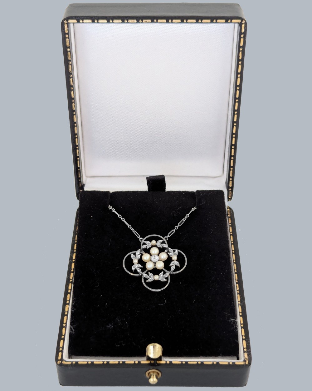 An Edwardian openwork platinum pendant featuring a central diamond encircled by pearls and leaf motifs, suspended on a fine platinum chain. View VI
