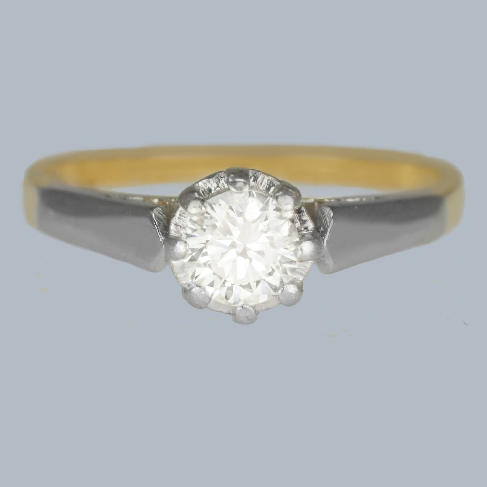 An Art Deco diamond solitaire ring featuring a round central diamond held in a platinum setting on an 18ct yellow gold band.