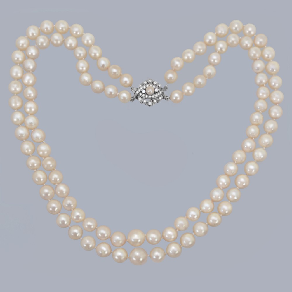 A vintage double strand cream pearl necklace featuring an ornate 9ct white gold foliate clasp set with small diamonds.