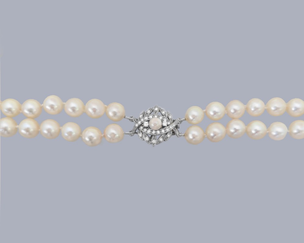 A vintage double strand cream pearl necklace featuring an ornate 9ct white gold foliate clasp set with small diamonds. View V