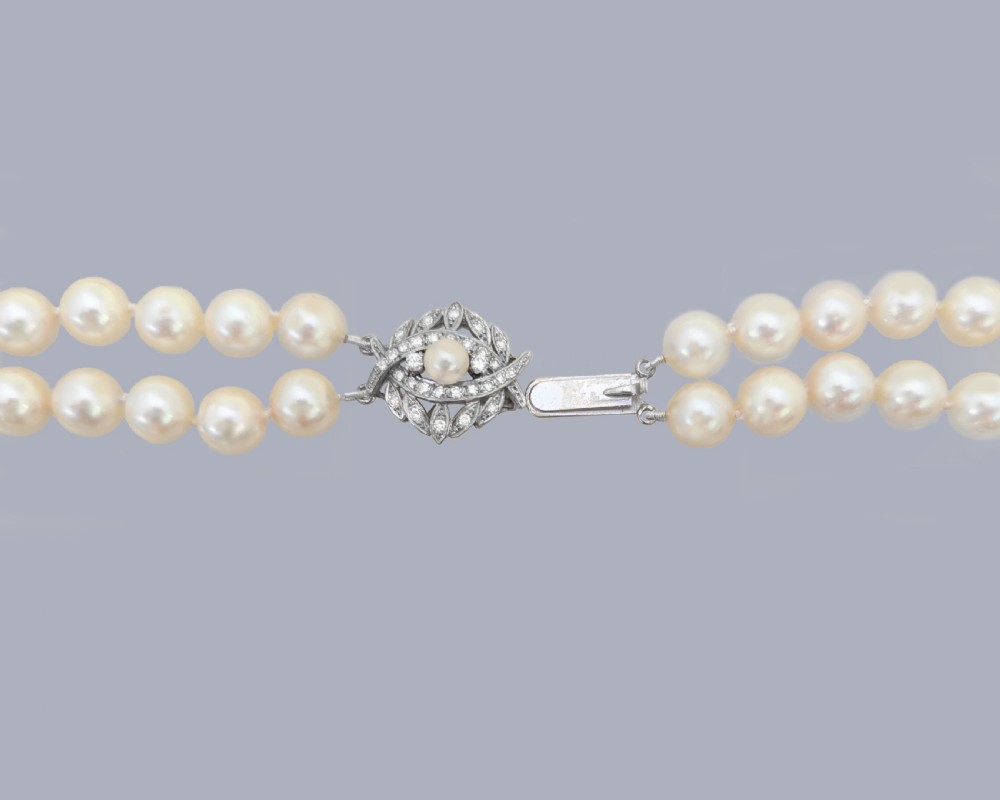 A vintage double strand cream pearl necklace featuring an ornate 9ct white gold foliate clasp set with small diamonds. View VI