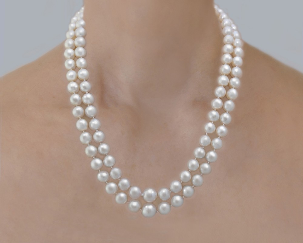 A vintage double strand cream pearl necklace featuring an ornate 9ct white gold foliate clasp set with small diamonds. View X