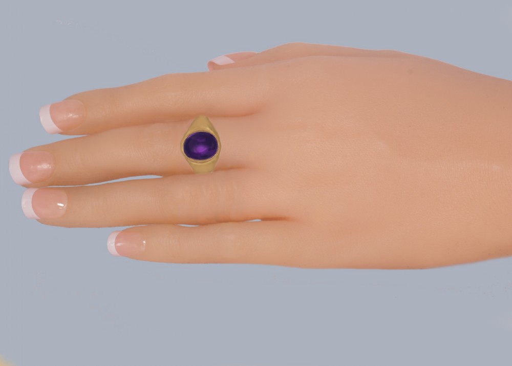 A 9ct yellow gold signet style ring featuring a central oval cabochon cut purple amethyst set in a smooth bezel setting. View III