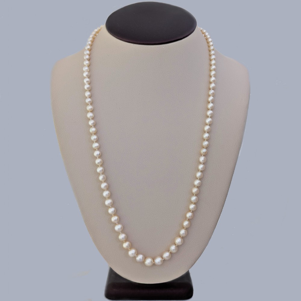 A long single strand of graduated white cultured pearls featuring an 18ct gold clasp with a dark accent pearl and safety chain. View II
