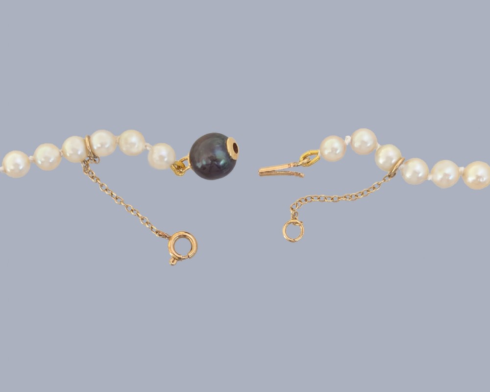 A long single strand of graduated white cultured pearls featuring an 18ct gold clasp with a dark accent pearl and safety chain. View III
