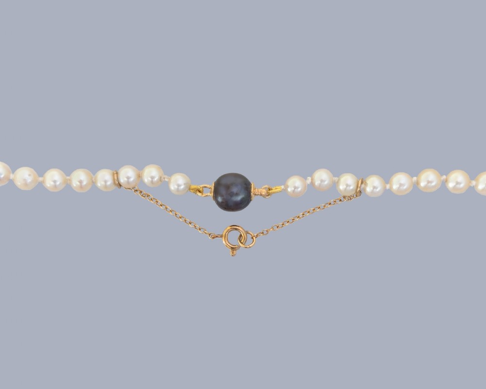 A long single strand of graduated white cultured pearls featuring an 18ct gold clasp with a dark accent pearl and safety chain. View IV
