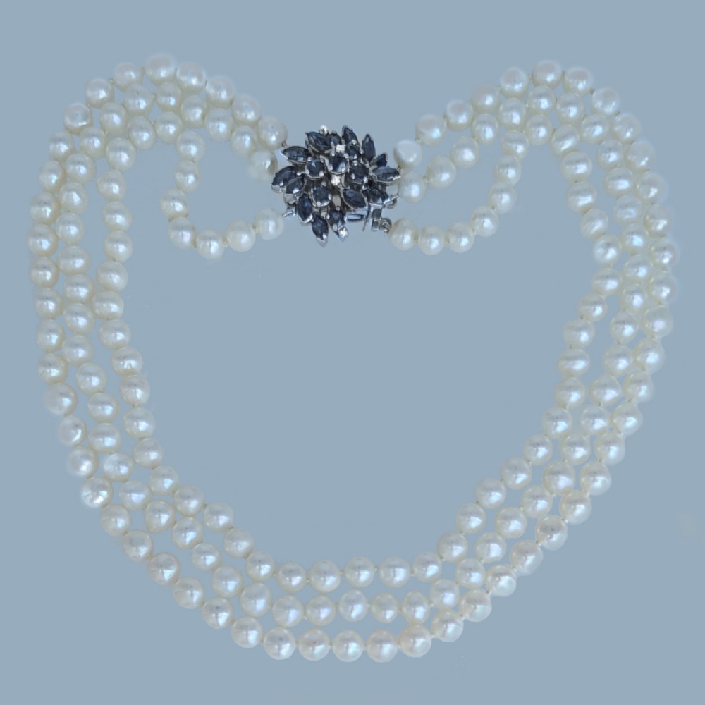 A vintage three-strand white pearl necklace joined by a silver floral clasp set with marquise-cut blue sapphires and small diamonds.