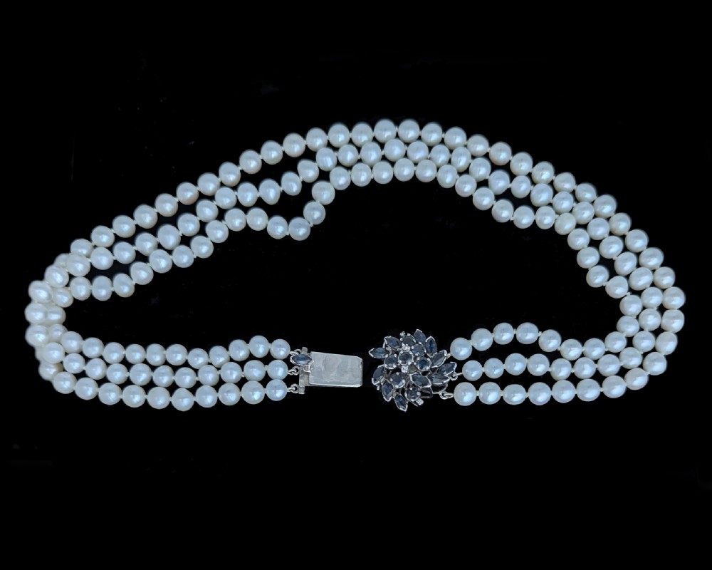 A vintage three-strand white pearl necklace joined by a silver floral clasp set with marquise-cut blue sapphires and small diamonds. View VII