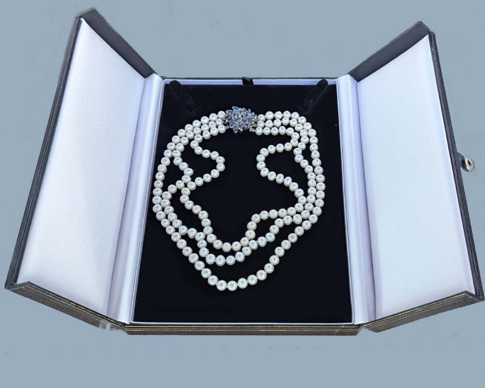 A vintage three-strand white pearl necklace joined by a silver floral clasp set with marquise-cut blue sapphires and small diamonds. View IX