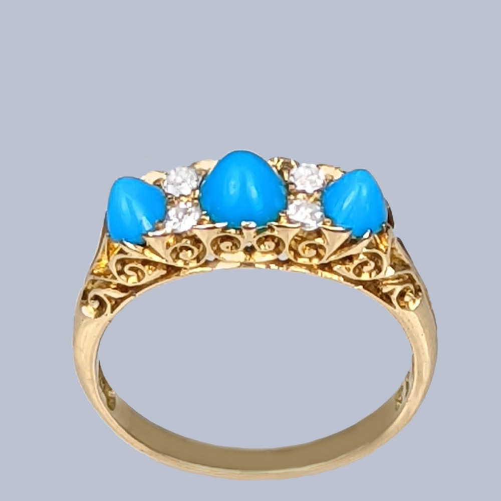 An 18ct yellow gold late Victorian ring featuring three dome-shaped blue turquoise cabochons accented by small old cut diamonds set within a carved scrollwork gallery.