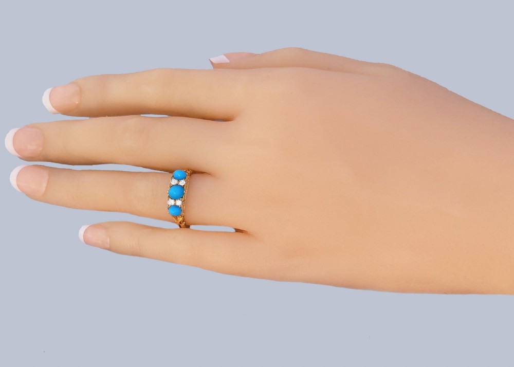 An 18ct yellow gold late Victorian ring featuring three dome-shaped blue turquoise cabochons accented by small old cut diamonds set within a carved scrollwork gallery. View VIII