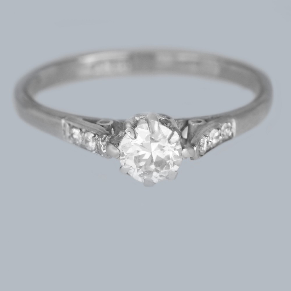 An 18ct white gold solitaire ring showcasing a central round diamond in a claw setting flanked by small diamonds in the shoulders. View II