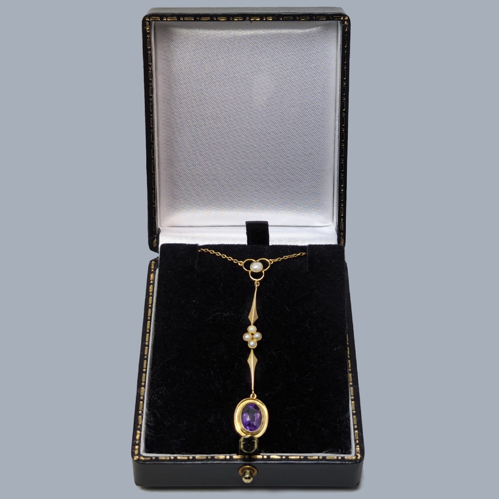 An Edwardian 9ct gold drop necklace featuring a fine chain suspending an elongated linear pendant set with seed pearls and an oval-cut amethyst. View VI