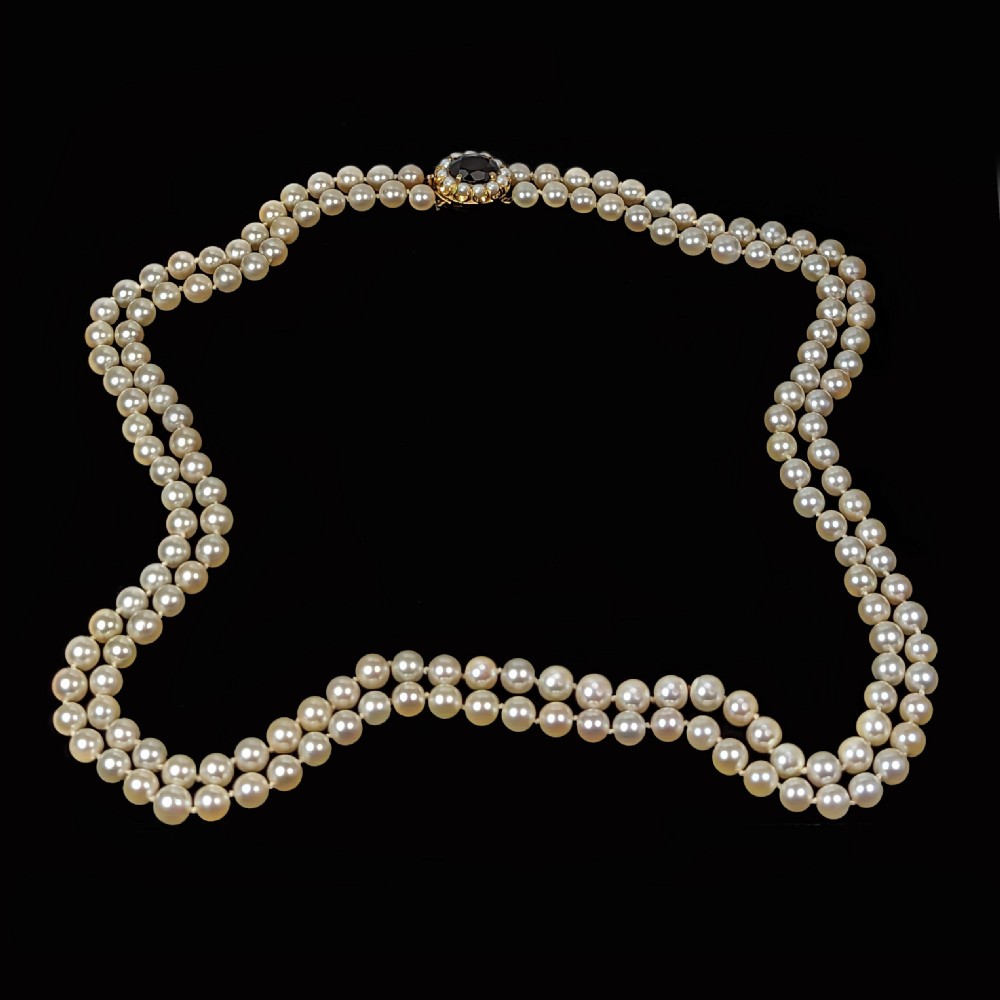 A double strand cultured pearl necklace featuring uniform cream pearls fastened with a round 9ct gold clasp inset with a dark red garnet stone. View V