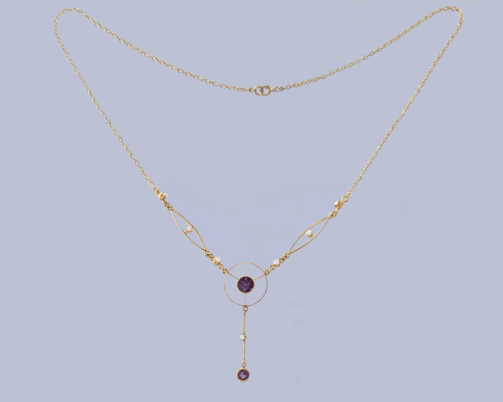 An Edwardian 18ct gold lavalier necklace featuring openwork geometric wire loops set with small diamonds, a central round bezel-set amethyst, and a vertical drop terminating in a second amethyst stone. View VII