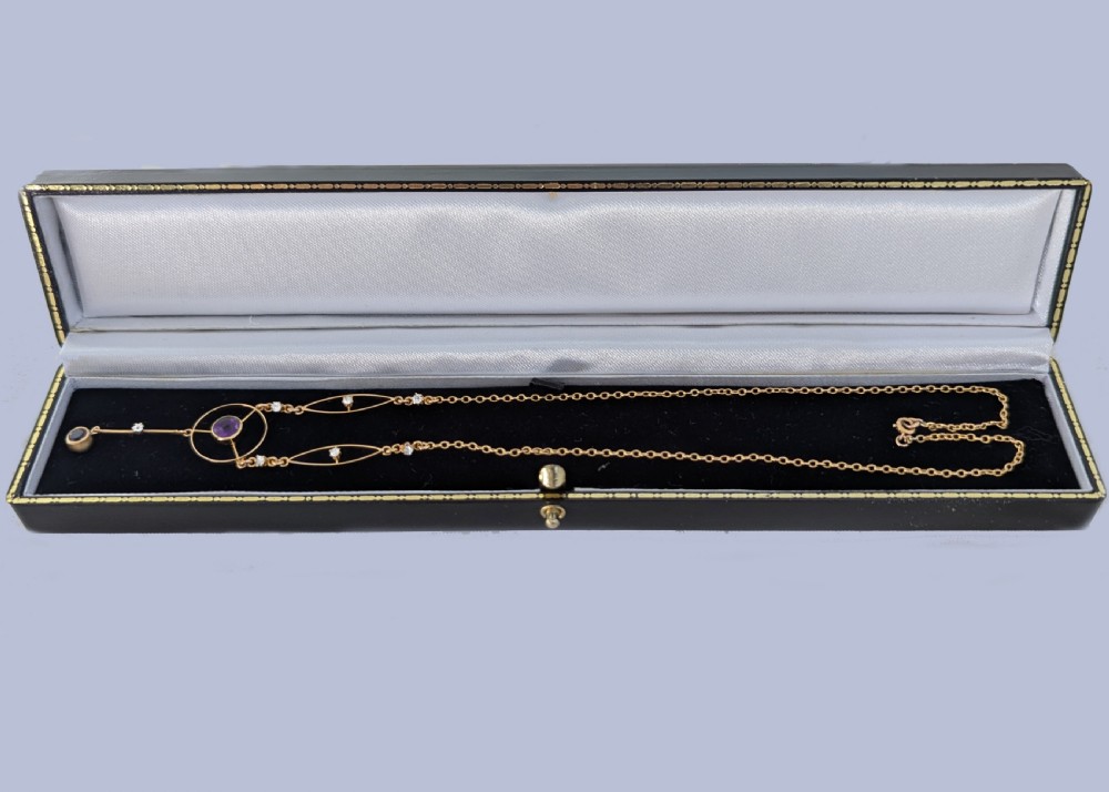 An Edwardian 18ct gold lavalier necklace featuring openwork geometric wire loops set with small diamonds, a central round bezel-set amethyst, and a vertical drop terminating in a second amethyst stone. View IX