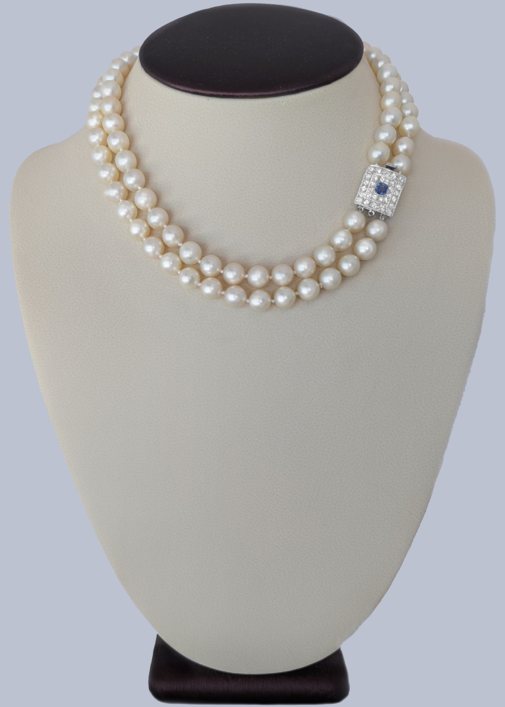 A double strand cream pearl necklace featuring a square 18ct white gold clasp set with a central square blue sapphire and accent diamonds. View IV