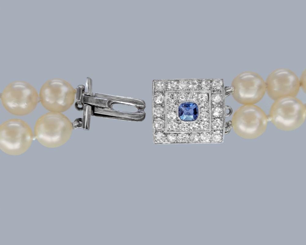 A double strand cream pearl necklace featuring a square 18ct white gold clasp set with a central square blue sapphire and accent diamonds. View V