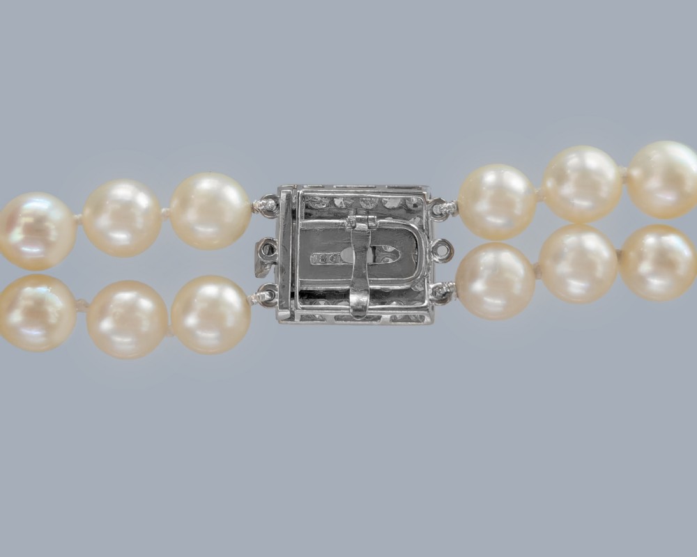 A double strand cream pearl necklace featuring a square 18ct white gold clasp set with a central square blue sapphire and accent diamonds. View VI