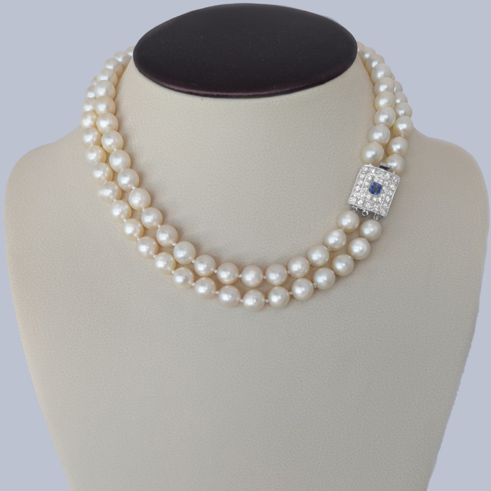 A double strand cream pearl necklace featuring a square 18ct white gold clasp set with a central square blue sapphire and accent diamonds. View XI