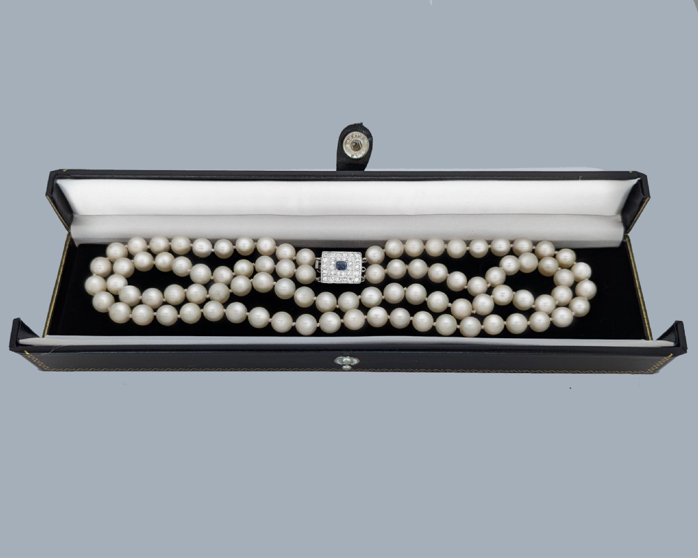 A double strand cream pearl necklace featuring a square 18ct white gold clasp set with a central square blue sapphire and accent diamonds. View XVI