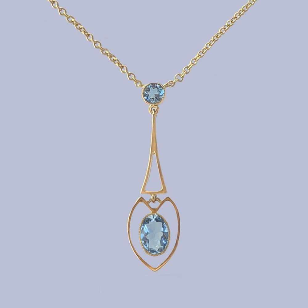 An Edwardian 15ct yellow gold drop pendant featuring a round aquamarine stone above an openwork heart-shaped frame housing an oval aquamarine gemstone on a fine link chain.