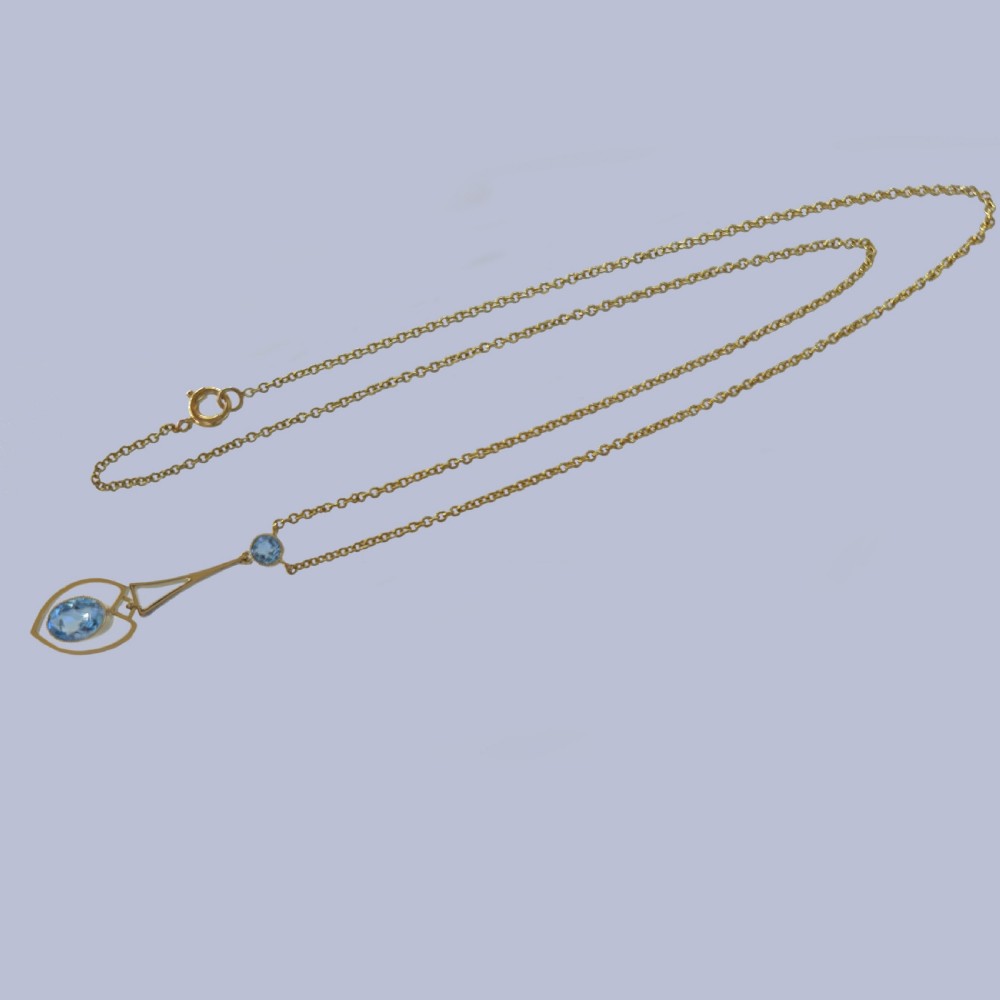 An Edwardian 15ct yellow gold drop pendant featuring a round aquamarine stone above an openwork heart-shaped frame housing an oval aquamarine gemstone on a fine link chain. View III
