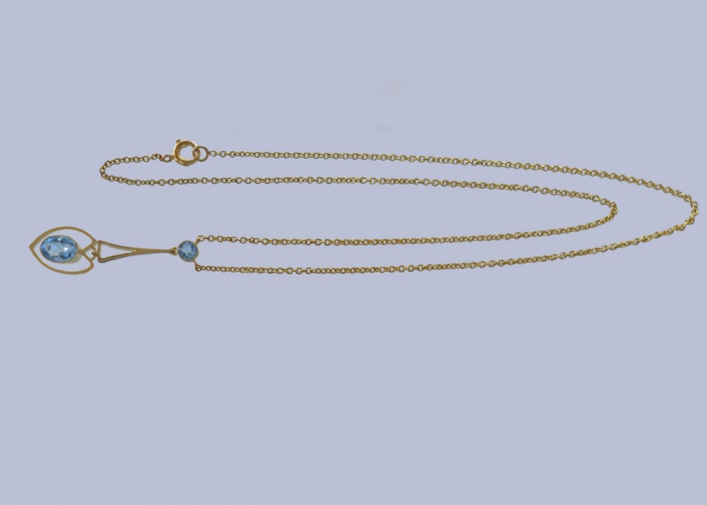 An Edwardian 15ct yellow gold drop pendant featuring a round aquamarine stone above an openwork heart-shaped frame housing an oval aquamarine gemstone on a fine link chain. View XI