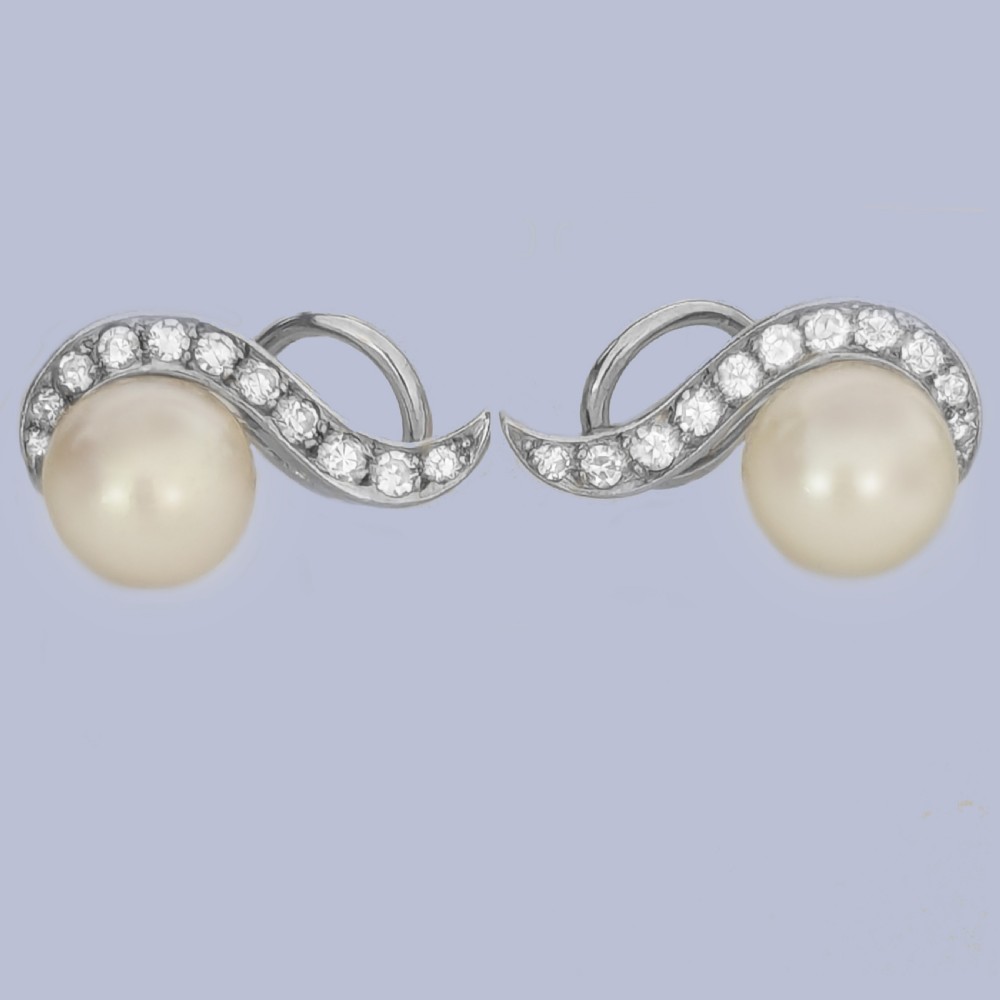 A pair of 18ct white gold stud earrings featuring round cream pearls accented with sweeping bands of grain-set diamonds. View IV