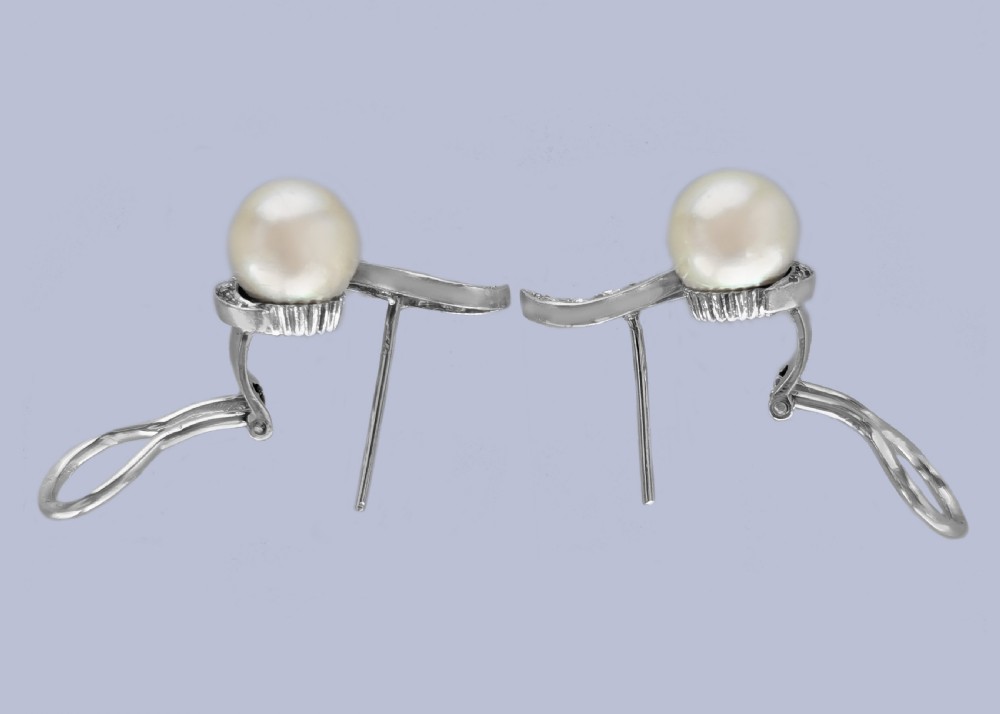 A pair of 18ct white gold stud earrings featuring round cream pearls accented with sweeping bands of grain-set diamonds. View VII