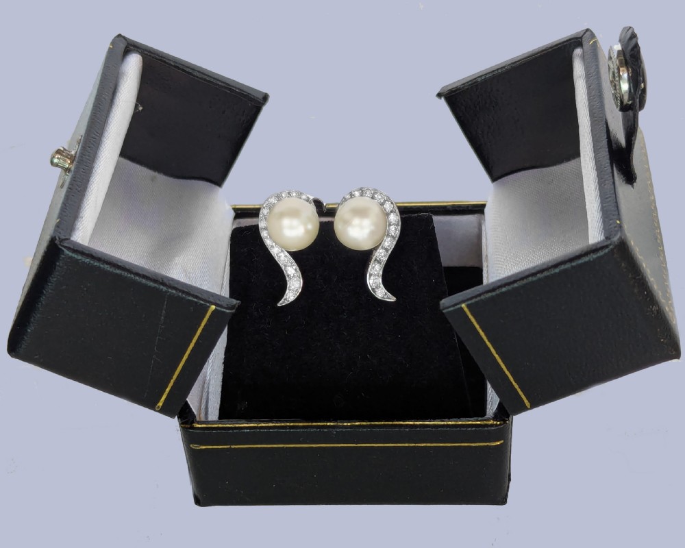 A pair of 18ct white gold stud earrings featuring round cream pearls accented with sweeping bands of grain-set diamonds. View IX