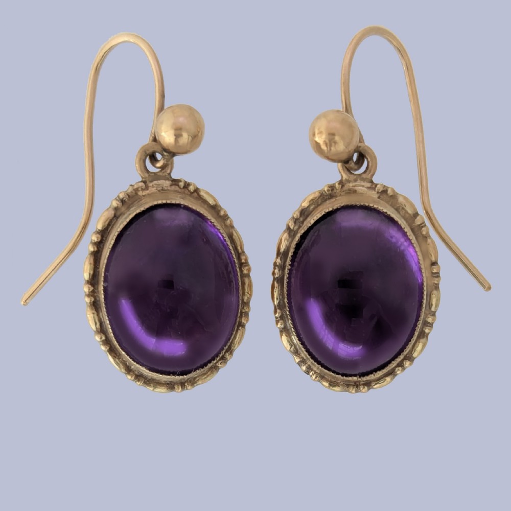 Pair of vintage 9ct gold drop earrings featuring oval cabochon purple amethysts set in decorative gold borders with shepherds hook wires.
