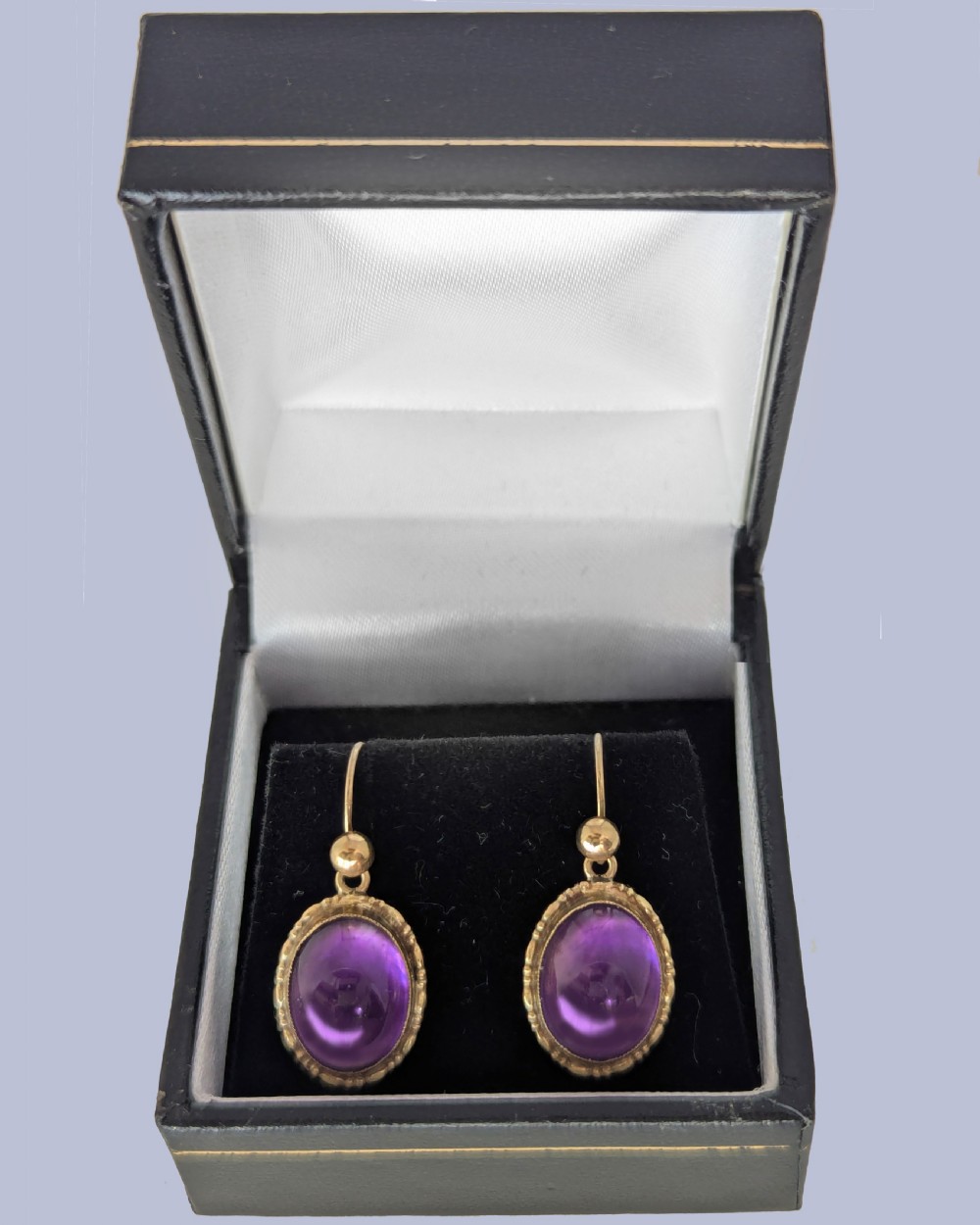 Pair of vintage 9ct gold drop earrings featuring oval cabochon purple amethysts set in decorative gold borders with shepherds hook wires. View IV