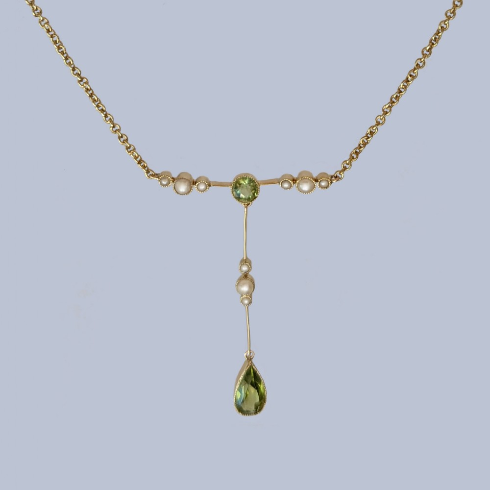 An Edwardian 15ct gold lavalier pendant necklace featuring a central round peridot, seed pearl accents, and a suspended pear-cut peridot drop.
