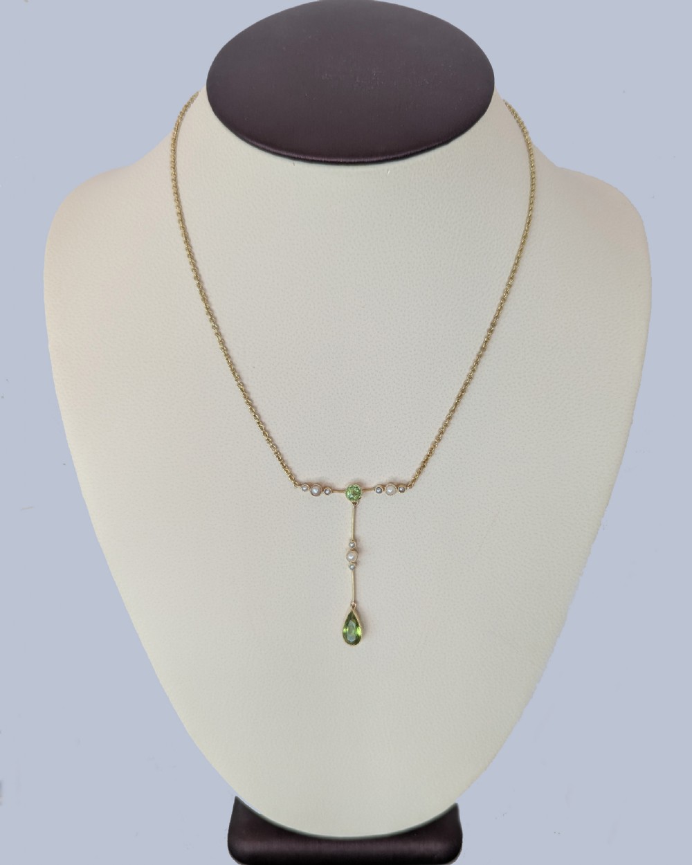 An Edwardian 15ct gold lavalier pendant necklace featuring a central round peridot, seed pearl accents, and a suspended pear-cut peridot drop. View II