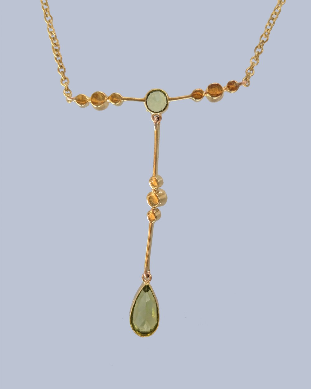 An Edwardian 15ct gold lavalier pendant necklace featuring a central round peridot, seed pearl accents, and a suspended pear-cut peridot drop. View V