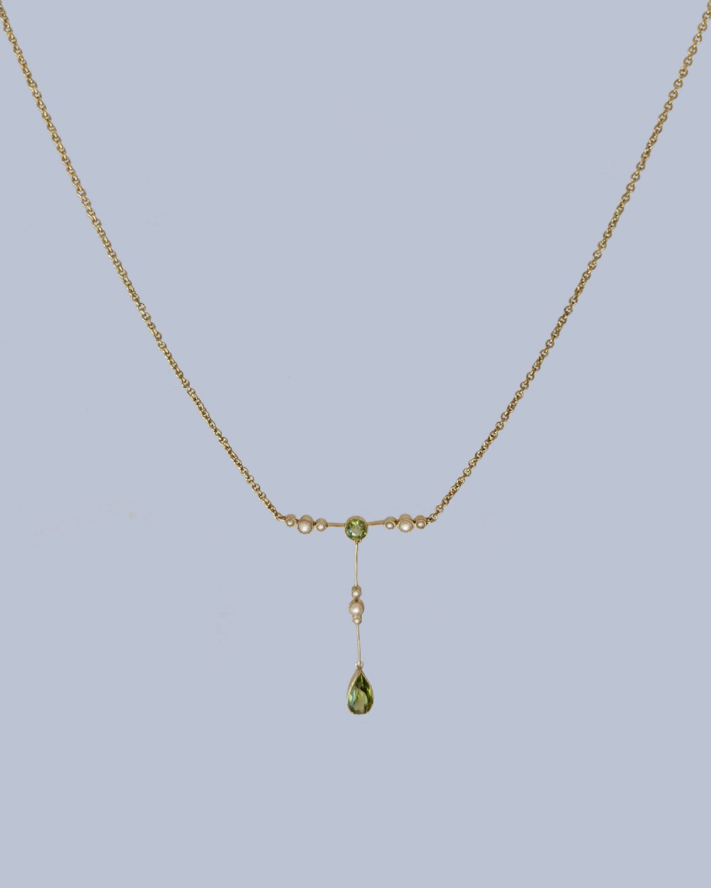 An Edwardian 15ct gold lavalier pendant necklace featuring a central round peridot, seed pearl accents, and a suspended pear-cut peridot drop. View VII
