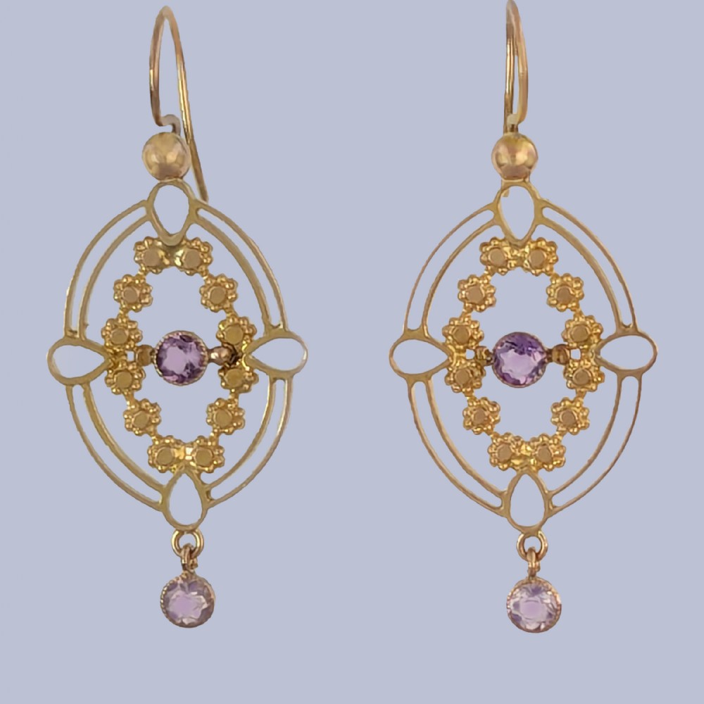 A pair of Edwardian 9ct gold drop earrings featuring an openwork oval frame, a central round amethyst, floral details, and a dangling amethyst bottom drop.