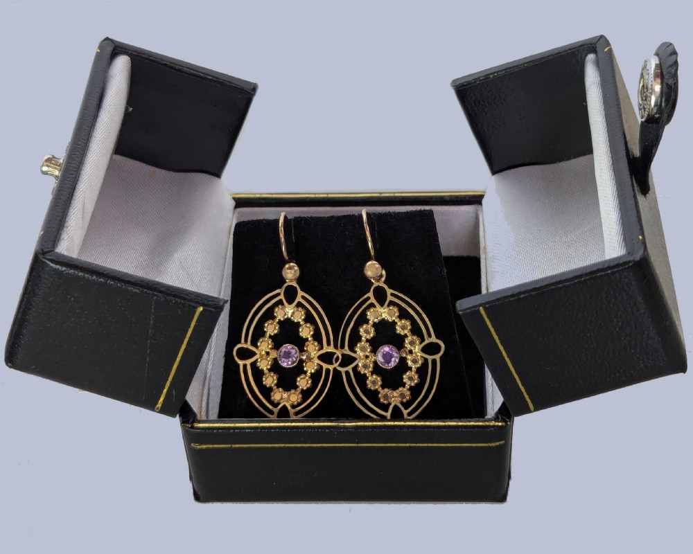 A pair of Edwardian 9ct gold drop earrings featuring an openwork oval frame, a central round amethyst, floral details, and a dangling amethyst bottom drop. View IV