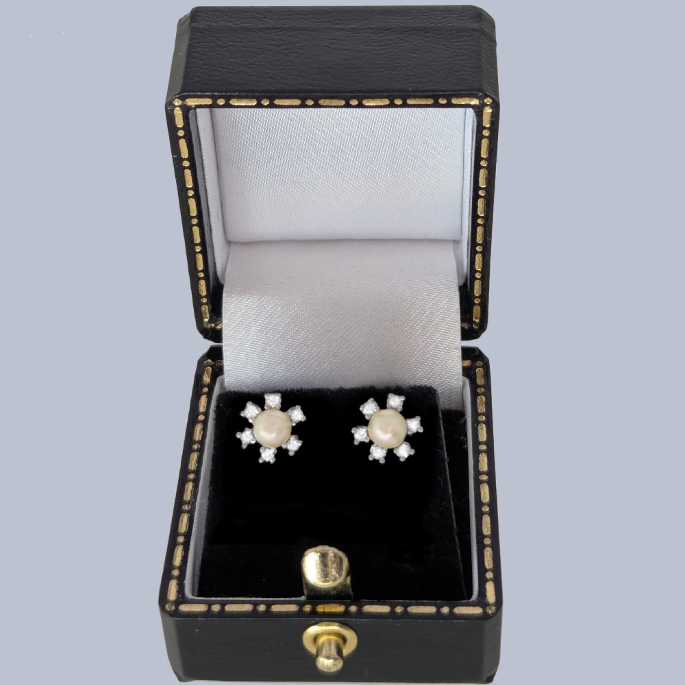 A pair of 18ct white gold stud earrings featuring a central cream pearl surrounded by six claw-set diamonds in a floral cluster arrangement. View VI