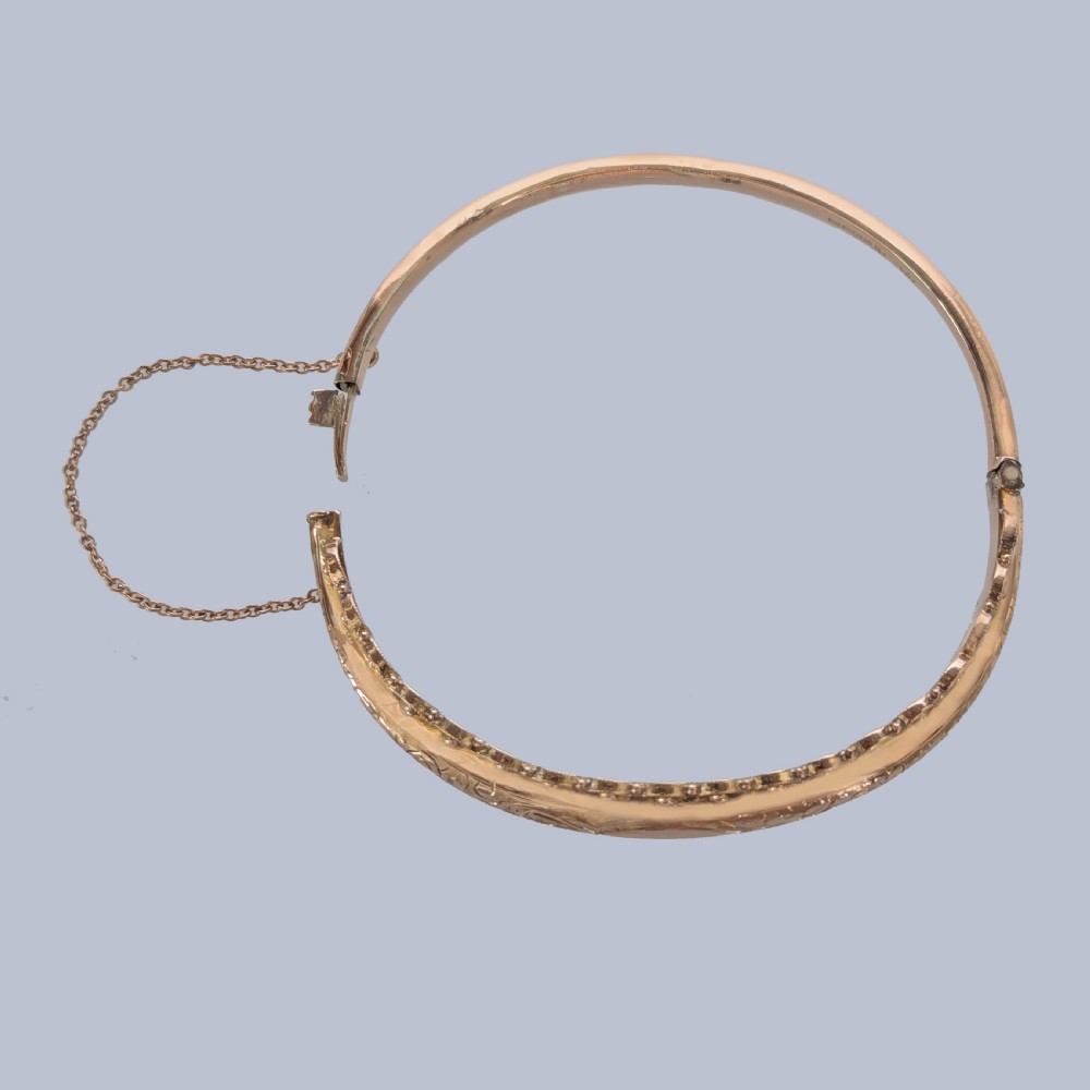 An Edwardian 9ct rose gold hinged bangle with foliate engraving, beaded border trim, and a safety chain. View VII